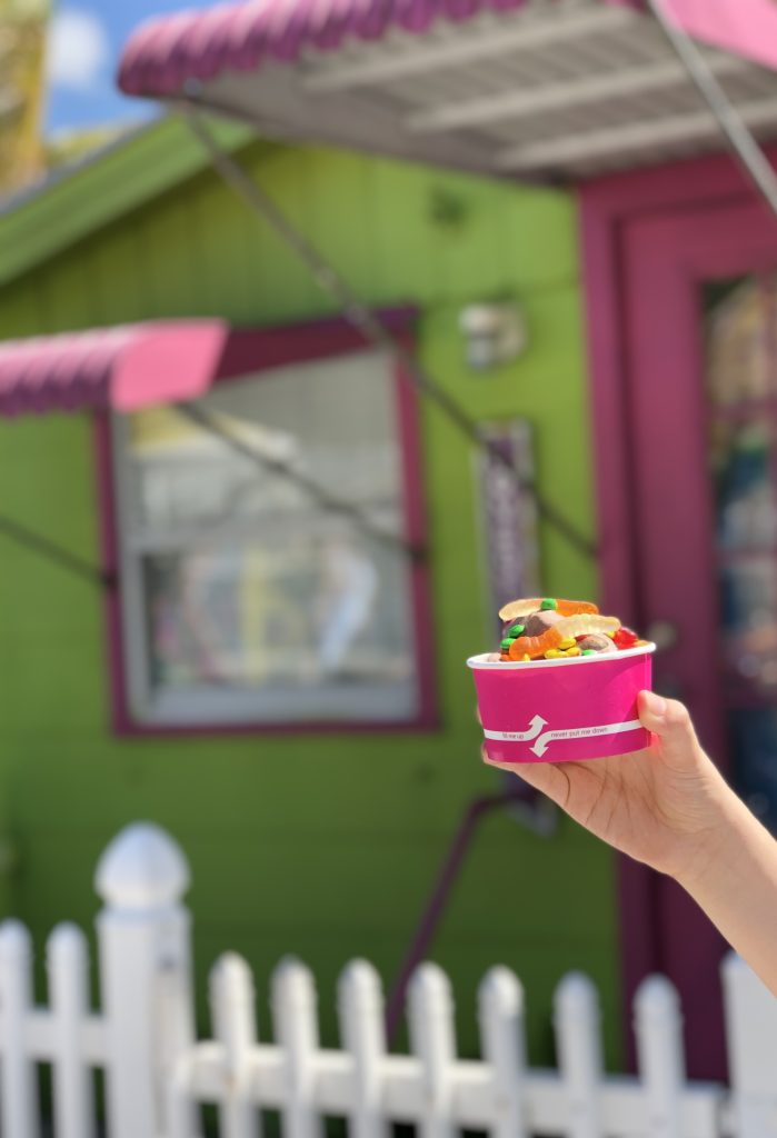Cup of ice cream held in front of a bright green and pink building in Matlacha Florida.