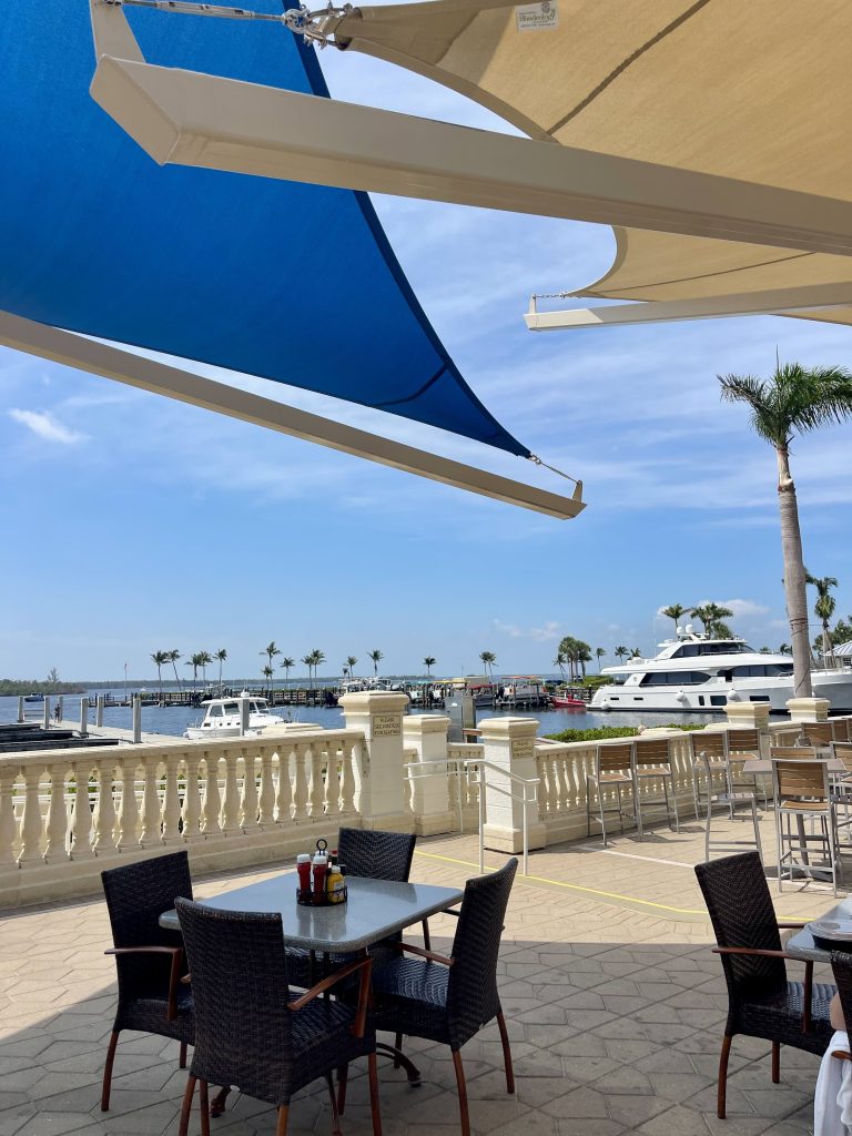 Outdoor patio seating at Marker 92 in Cape Coral with views of Tarpon Point Marina, boats, palm trees, and waterfront dining tables