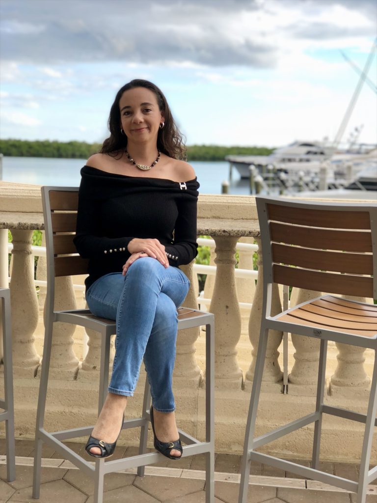 Woman seated on the outdoor patio at Marker 92 in Cape Coral with Tarpon Point Marina and boats in the background