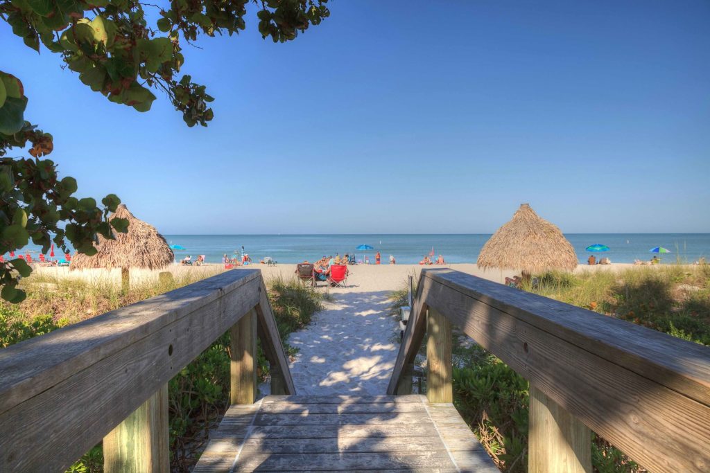 Wooden beach access walkway leading to Lowdermilk Beach in Naples Florida with tiki huts and Gulf water