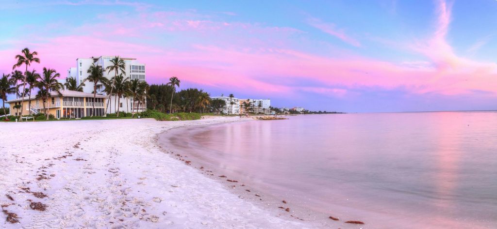 Lowdermilk Beach in Naples Florida at sunset with white sand, calm Gulf water and pastel pink sky