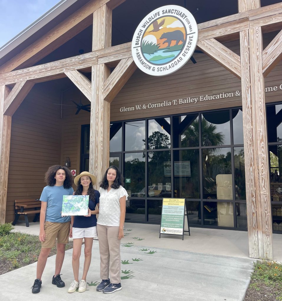 Family standing in front of Busch Wildlife Sanctuary holding a painting made by Charlie the Florida panther.