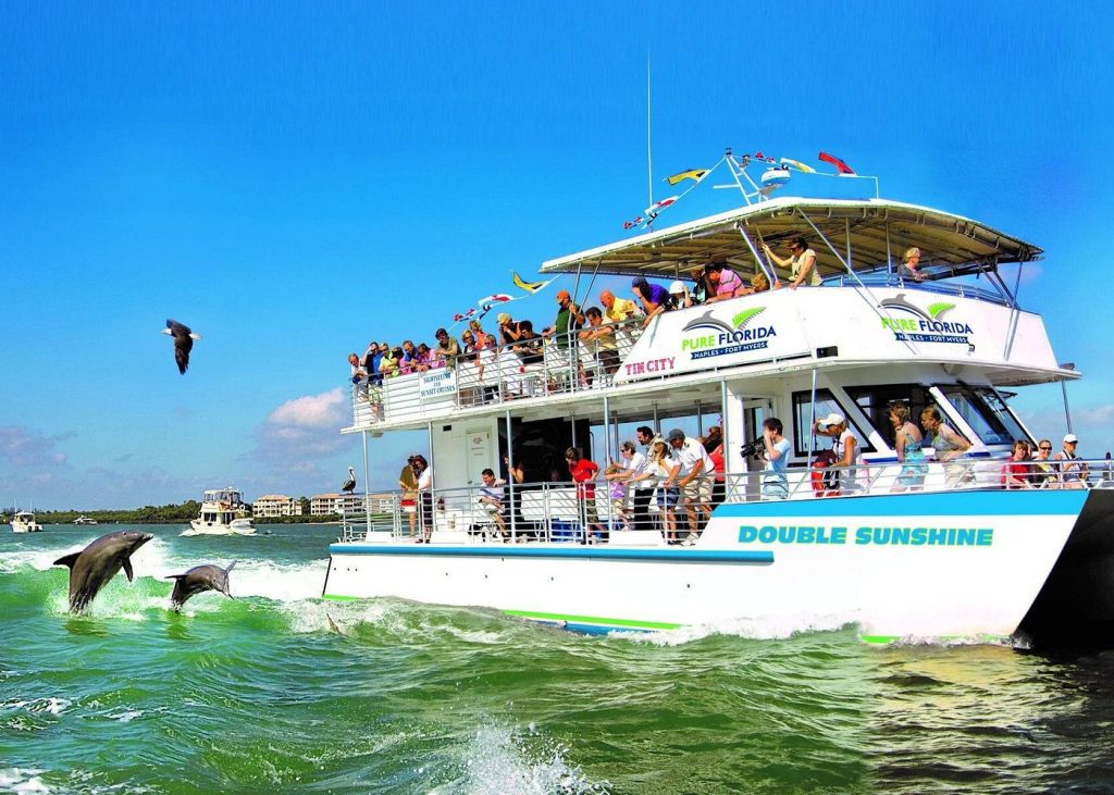 Pure Florida dolphin tour boat with dolphins jumping alongside in Naples Florida